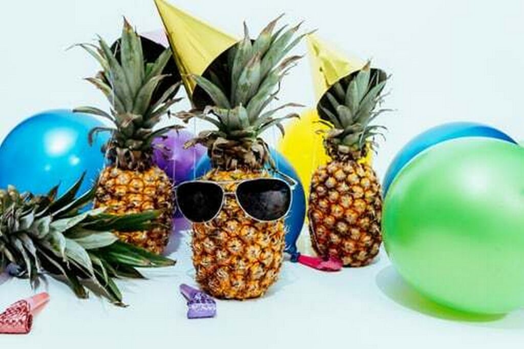 A pinaple with sunglasses surrounded by balloons