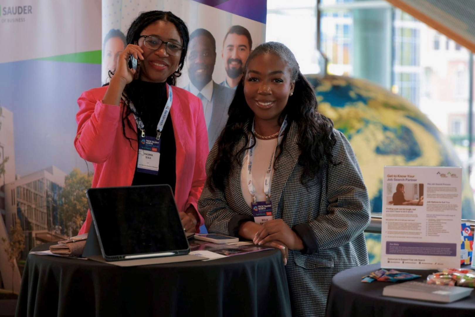 two black women smiling together, standing at a trade show booth