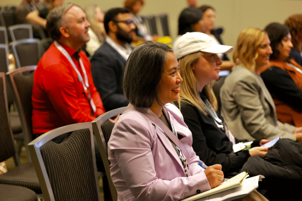 people sitting in conference chairs, smiling and listing to a presenter