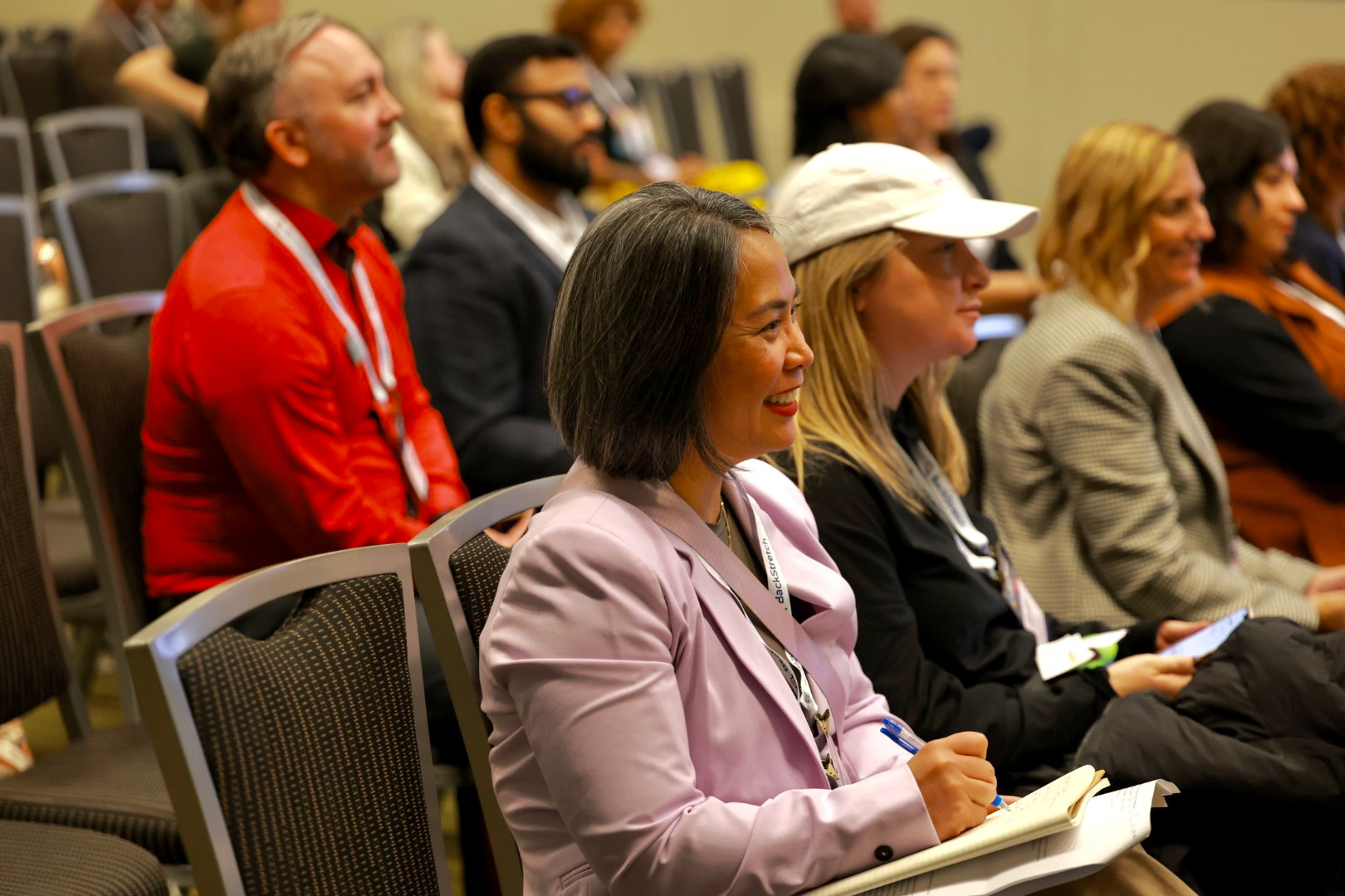 people sitting in conference chairs, smiling and listing to a presenter