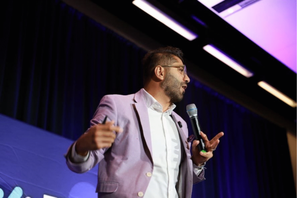 a man presenting on stage, holding a microphone and gesturing with his arms as he speaks
