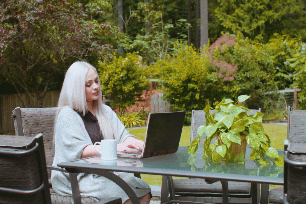 Woman sitting at a garden table, working on a laptop,