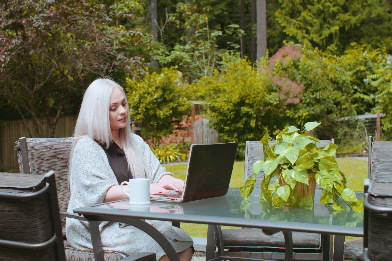 Woman sitting at a garden table, working on a laptop,