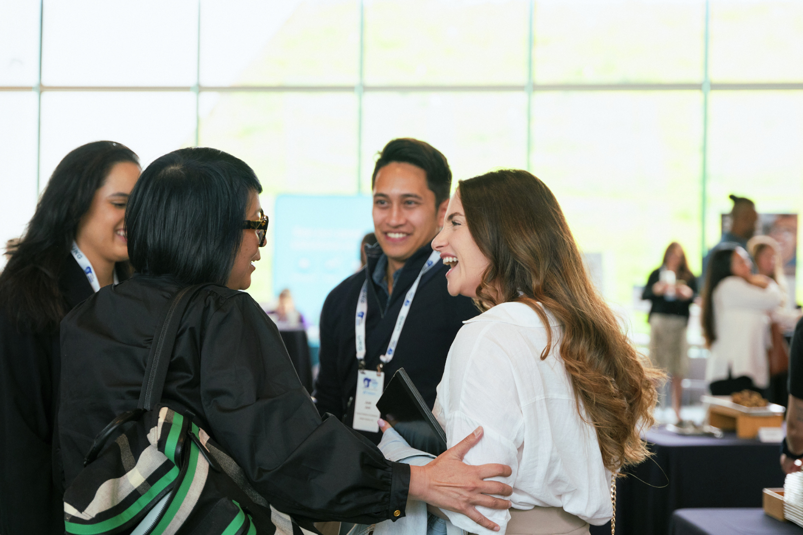 Four people smiling and talking together. One has her arm on another, in way of greeting