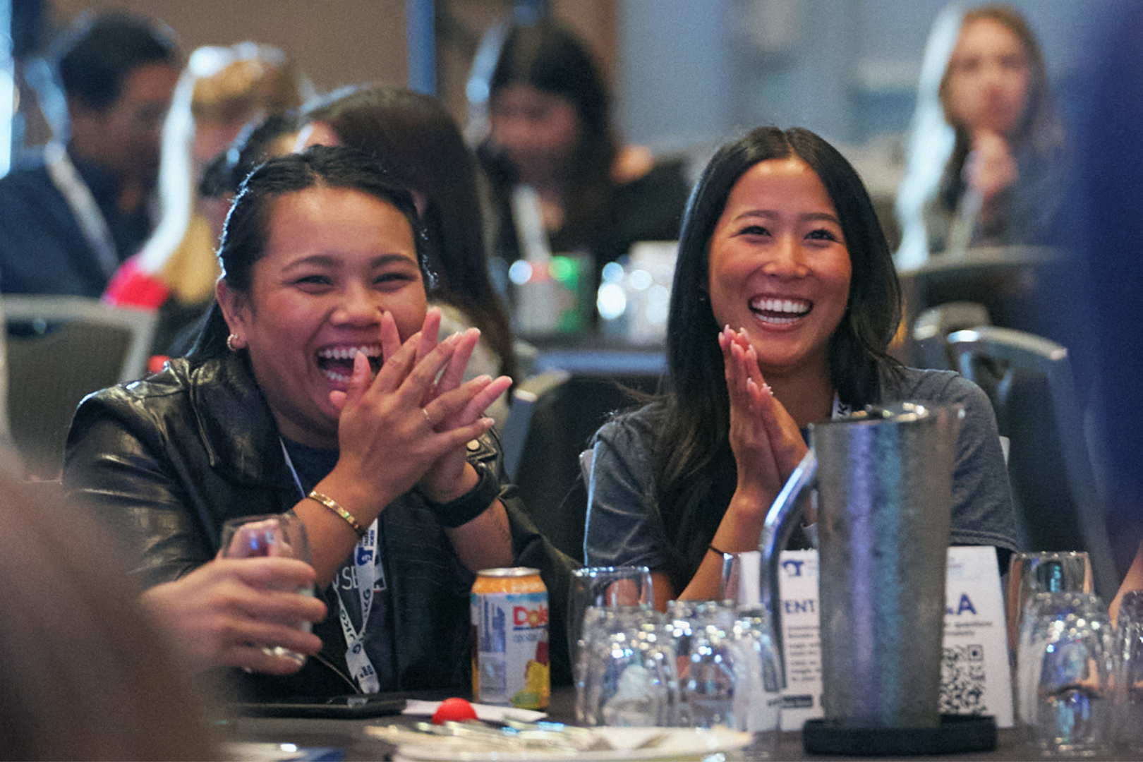 two woman sitting at a table during a conference, laughing and clapping