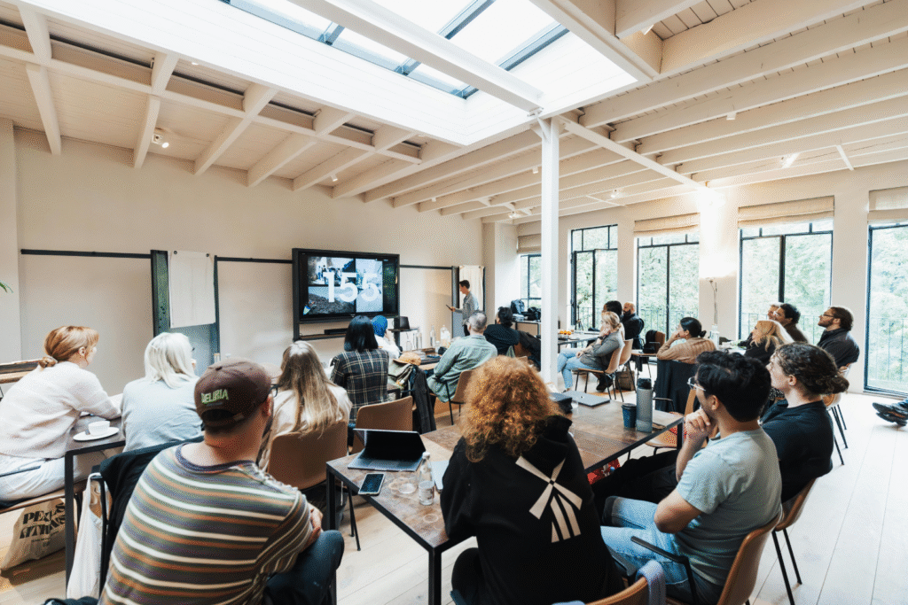 people in a classroom setting, watching a large monitor