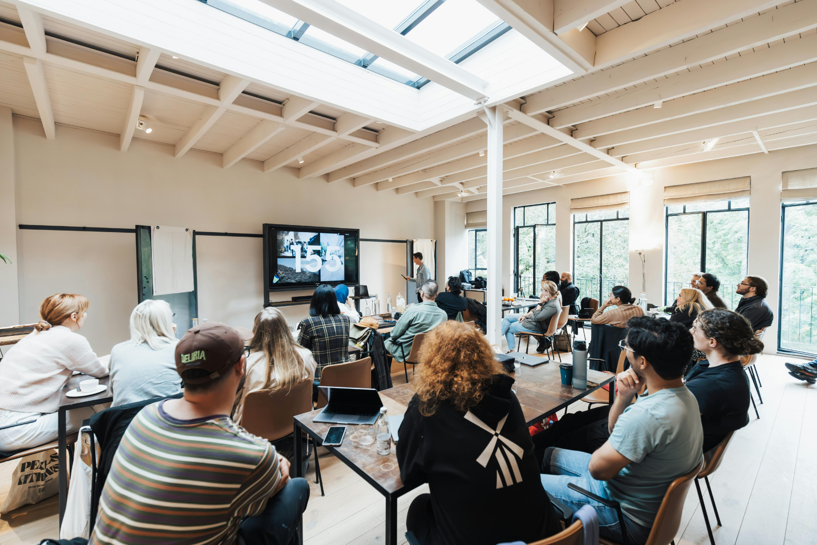 people in a classroom setting, watching a large monitor