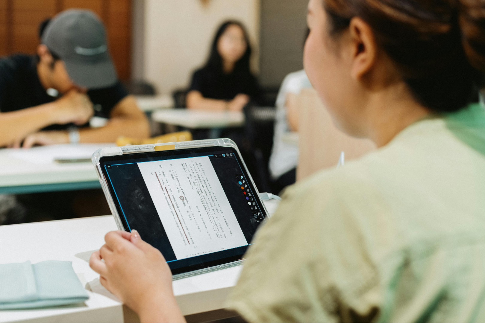 a woman holding an iPad, with others in the background, blurred out