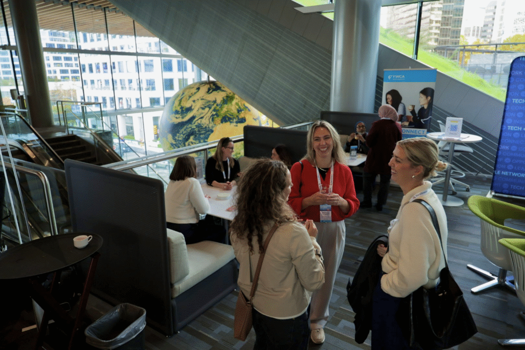 three woman standing at a conference, talking and laughing together.