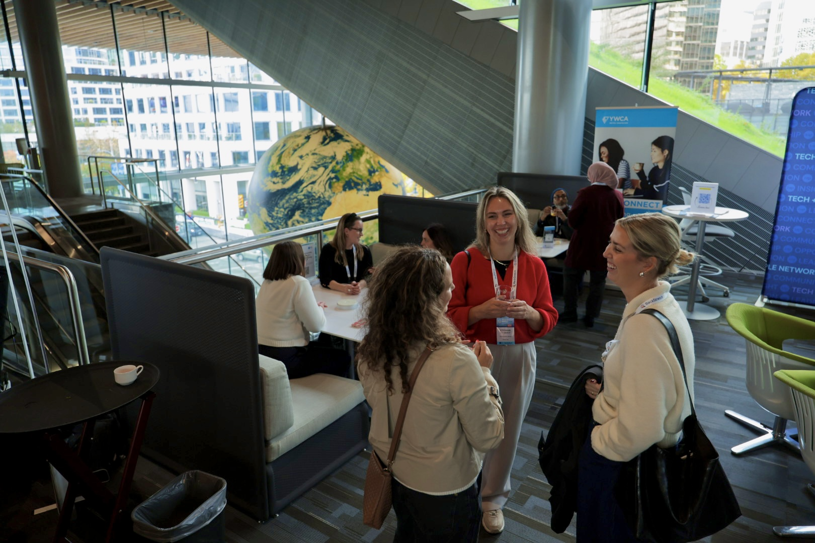 three woman standing at a conference, talking and laughing together.